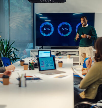 Multiracial business team having a meeting in a modern bright office interior while an african american man tam leader present project to its diverse colleagues. Using a diagrams on a big screen.
